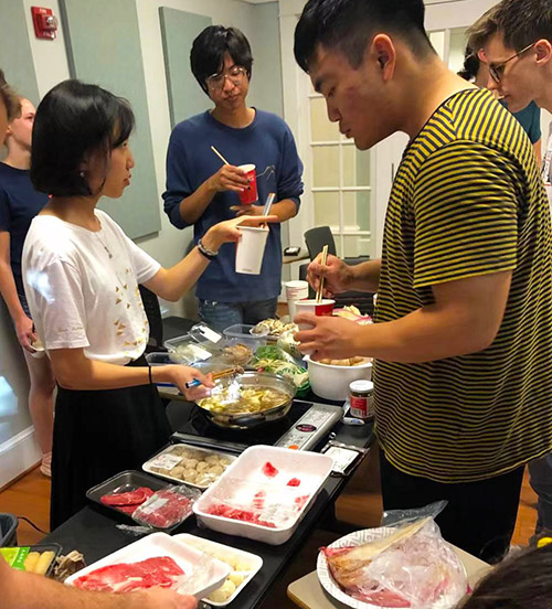 Students standing around a table with meat and vegetables to cook in hot pot