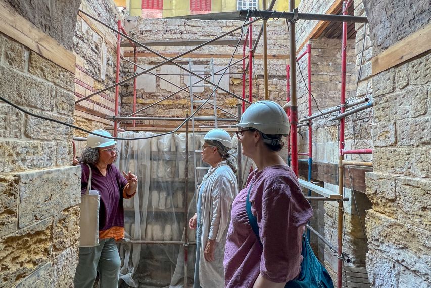 Three people in hard hats under an archway. One is gesturing. Old Cairene building is in the background.
