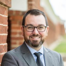 Tim Troy headshot wearing glasses and grey suit